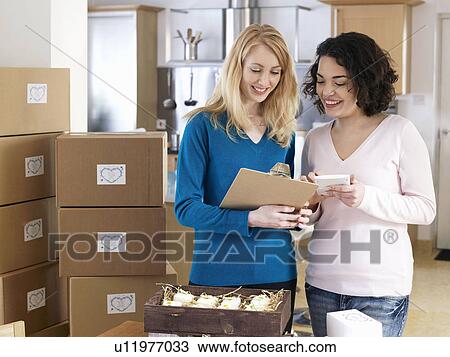 Stock Image - Two women with boxes in kitchen. Fotosearch