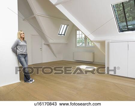 Stock Image - Woman leaning against wall in empty white loft.. Fotosearch