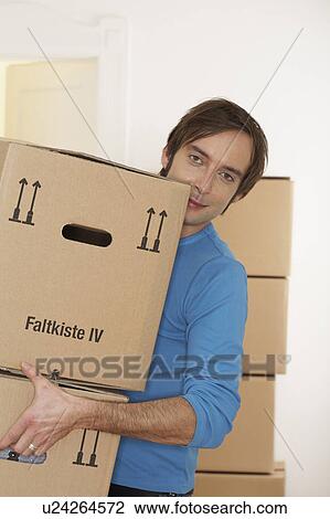 Stock Image - Young man carrying packing cases smiling, portrait. Fotosearch