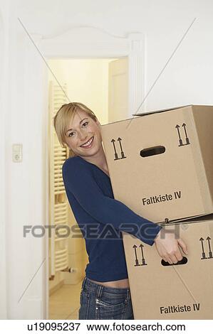 Stock Photo - Young woman carrying packing cases smiling, portrait. Fotosearch