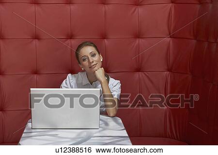 Stock Photograph - Businesswoman working at a table with red seating. Fotosearch
