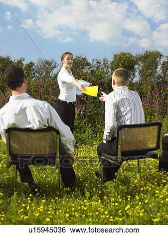 Stock Photograph - Group of businesspeople sitting on chairs in field.. Fotosearch