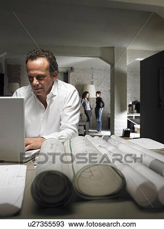 Architect working on laptop, two females in background. Brussels, Belgium. View Large Photo Image Stock Image - Architect working on laptop, two females in background. Brussels, Belgium.. Fotosearch