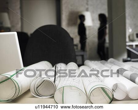 Stock Image - Blueprints on desk, two architects in background. Brussels, Belgium.. Fotosearch