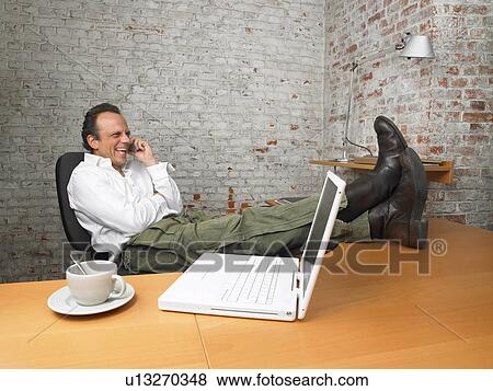 Businessman laughing on the phone, feet on desk., Brussels, Belgium. View Large Photo Image Stock Photo - Businessman laughing on the phone, feet on desk., Brussels, Belgium.. Fotosearch