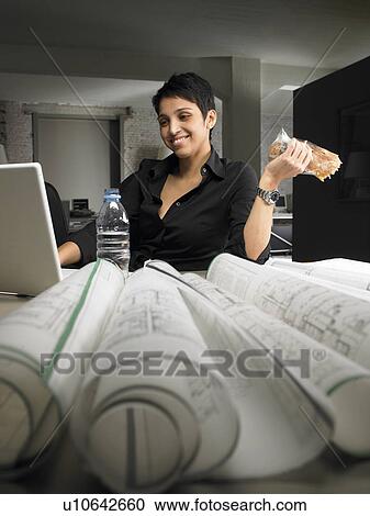 Female architect having snack while reading blueprint at desk. Brussels, Belgium. View Large Photo Image Stock Image - Female architect having snack while reading blueprint at desk. Brussels, Belgium.. Fotosearch