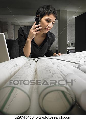 Female architect using mobile phone, looking at plans on desk View Large Photo Image Stock Photograph - Female architect using mobile phone, looking at plans on desk. Fotosearch