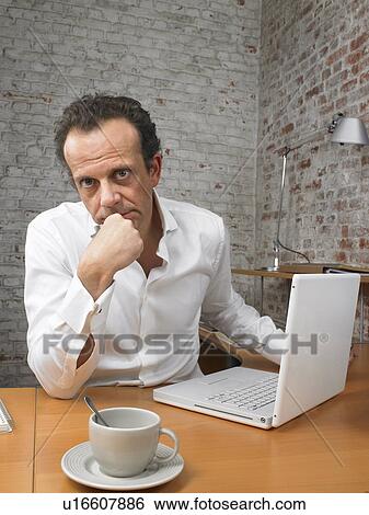 Pensive businessman sitting at desk looking at camera., Brussels, Belgium. View Large Photo Image Stock Photograph - Pensive businessman sitting at desk looking at camera., Brussels, Belgium.. Fotosearch