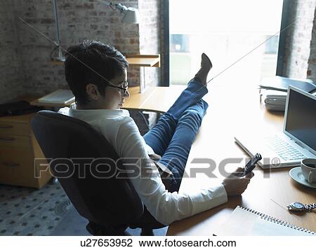 Rear view of businesswoman reading messages on phone with feet up on desk. Brussels, Belgium. View Large Photo Image Stock Image - Rear view of businesswoman reading messages on phone with feet up on desk. Brussels, Belgium.. Fotosearch