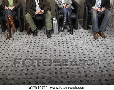 Stock Image - Two businesswomen and two businessmen sitting in waiting room, low section. Brussels, Belgium.. Fotosearch