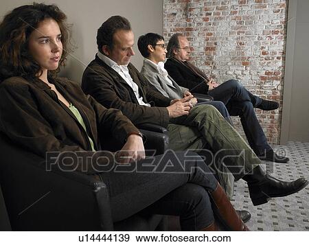 Stock Photo - Two businesswomen and two businessmen sitting in waiting room, side view. Brussels, Belgium.. Fotosearch