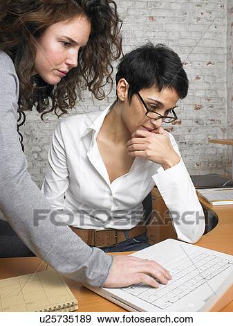 Stock Photo - Two businesswomen using laptop together in office. Fotosearch