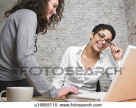 Two smiling businesswomen working on a laptop., Brussels, Belgium. View Large Photo Image Stock Photography - Two smiling businesswomen working on a laptop., Brussels, Belgium.. Fotosearch