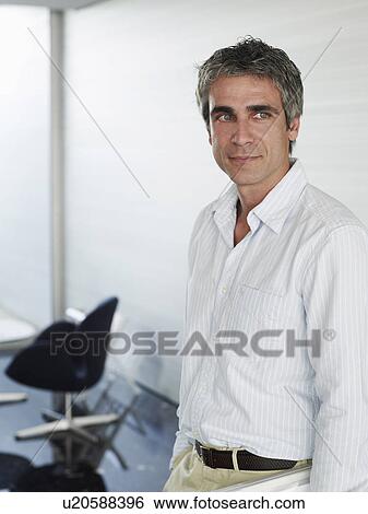 Stock Photograph - Businessman wearing open neck shirt standing in office. Fotosearch