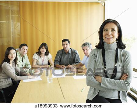 Stock Image - Businesswoman in meeting room, portrait, colleagues in background. Fotosearch