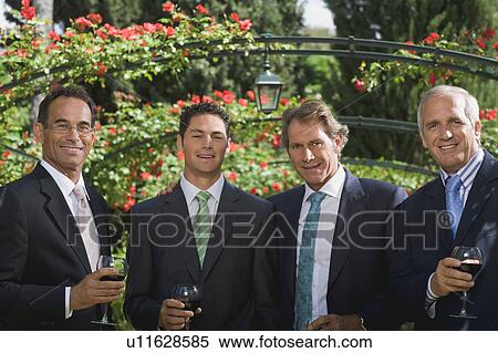 Stock Photography - Four businessmen drinking wine in a garden. Fotosearch