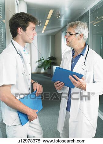 Mature doctor and young doctor in discussion in a lobby of a hospital. View Large Photo Image Stock Photography - Mature doctor and young doctor in discussion in a lobby of a hospital.. Fotosearch