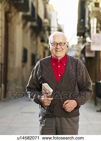 Stock Image - Senior man standing in street, smiling, portrait. Fotosearch