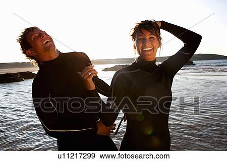 Couple in wetsuits laughing by the water. View Large Photo Image Stock Photo - Couple in wetsuits laughing by the water.. Fotosearch