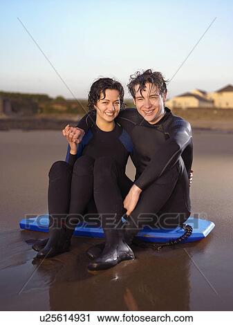 Couple in wetsuits sitting on body board. View Large Photo Image Stock Image - Couple in wetsuits sitting on body board.. Fotosearch