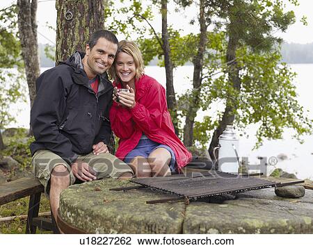 Stock Image - Couple sitting in a park by a fire pit smiling.. Fotosearch