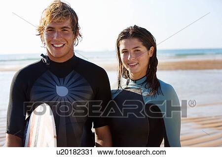 Couple standing with surfboard on beach smiling. View Large Photo Image Stock Image - Couple standing with surfboard on beach smiling.. Fotosearch