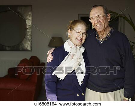 Picture - Senior couple standing in living room, smiling, portrait. Fotosearch