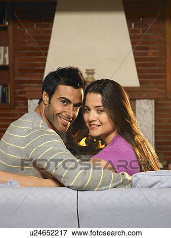 Stock Photo - Young couple relaxing in living room, smiling, portrait. Fotosearch