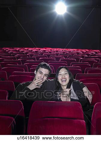 Stock Photo - Young couple sitting in empty cinema laughing, portrait. Fotosearch