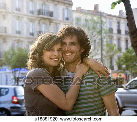 Stock Image - Young couple standing in street, smiling, portrait. Fotosearch
