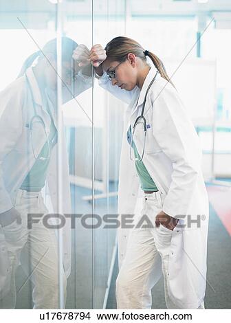 Concerned doctor leaning on glass wall in hospital lobby. View Large Photo Image Picture - Concerned doctor leaning on glass wall in hospital lobby.. Fotosearch
