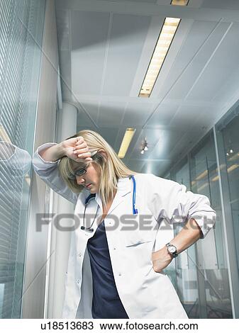 Concerned female doctor leaned on her forearm on glass wall in a lobby of a hospital. View Large Photo Image Stock Image - Concerned female doctor leaned on her forearm on glass wall in a lobby of a hospital.. Fotosearch