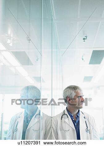 Concerned male doctor leaning on glass wall in hospital lobby. View Large Photo Image Stock Image - Concerned male doctor leaning on glass wall in hospital lobby.. Fotosearch