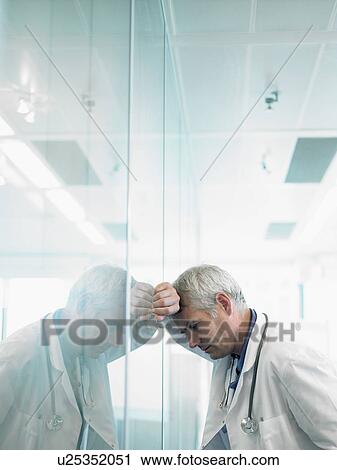 Concerned male doctor leaning on glass wall in hospital lobby. View Large Photo Image Stock Image - Concerned male doctor leaning on glass wall in hospital lobby.. Fotosearch