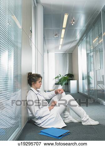 Stock Photo - Female doctor sitting on floor in hospital lobby.. Fotosearch