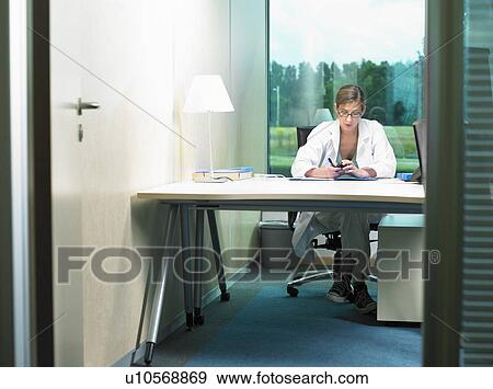 Female doctor working at her desk. View from opened door. View Large Photo Image Stock Photo - Female doctor working at her desk. View from opened door.. Fotosearch