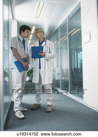 Mature doctor and young doctor in discussion in a lobby of a hospital. View Large Photo Image Stock Image - Mature doctor and young doctor in discussion in a lobby of a hospital.. Fotosearch