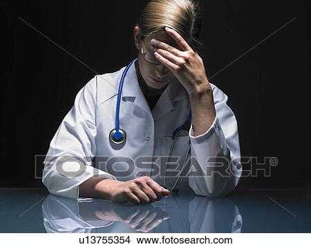 Portrait of concerned female doctor at her desk working late head in hand. View Large Photo Image Picture - Portrait of concerned female doctor at her desk working late head in hand.. Fotosearch