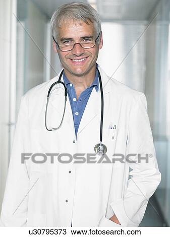 Stock Image - Portrait of mature male doctor in a lobby of a hospital. Close up smiling.. Fotosearch