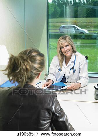 Smiling female doctor at her desk discussing with female patient. X rays on desk. View Large Photo Image Stock Photo - Smiling female doctor at her desk discussing with female patient. X rays on desk.. Fotosearch