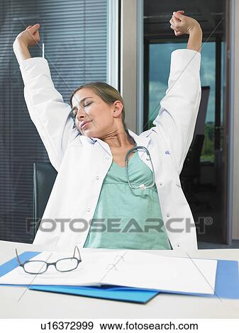 Stretching female doctor at her desk working late. View Large Photo Image Stock Photo - Stretching female doctor at her desk working late.. Fotosearch