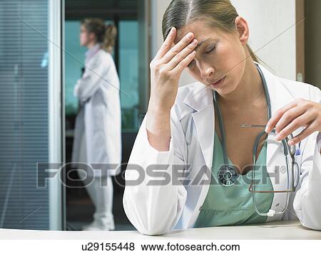 Tired doctor sitting at her desk with female doctor standing in the background. View Large Photo Image Stock Photo - Tired doctor sitting at her desk with female doctor standing in the background.. Fotosearch