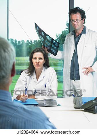 Two doctors discussing x-rays with mature patient. View Large Photo Image Picture - Two doctors discussing x-rays with mature patient.. Fotosearch