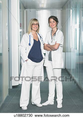 Two female doctors looking at camera in a lobby of a hospital smiling. View Large Photo Image Stock Image - Two female doctors looking at camera in a lobby of a hospital smiling.. Fotosearch