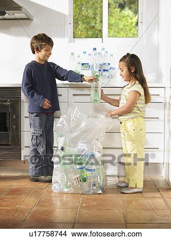 Picture - Boy (6-8) and girl (4-6) recycling bottles in kitchen. Fotosearch