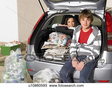 Stock Image - Brother 11-13) and sister (12-14) with car filled with recycling, portrait. Fotosearch