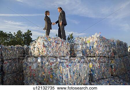 Stock Photography - Businessmen shaking hands at a recycling plant.. Fotosearch
