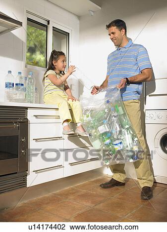 Stock Image - Father and daughter (4-6) sharing recycling duties in kitchen. Fotosearch