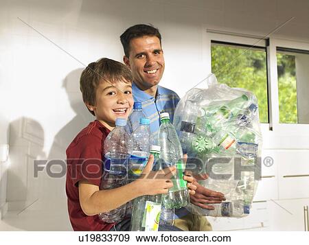 Stock Photo - Father and son (6-8) recycling plastic bottles, smiling. Fotosearch