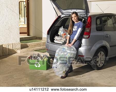 Stock Image - Girl (12-14) leaning on car holding recycling box, portrait. Fotosearch